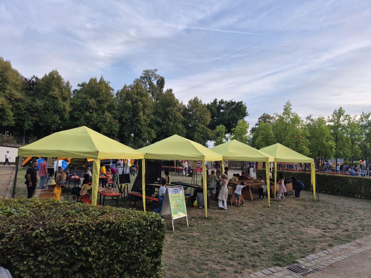 Der Spielepark mit vier gelben Pavillons, Holzspielen und vielen Kindern im Park