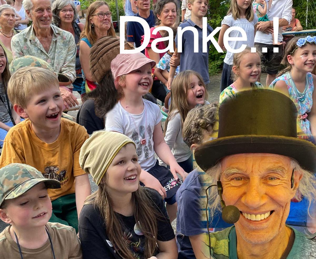 Lachende Kinder und Erwachsene im Publikum, vorne Micha mit Zylinder und Headset, darüber das Wort Danke