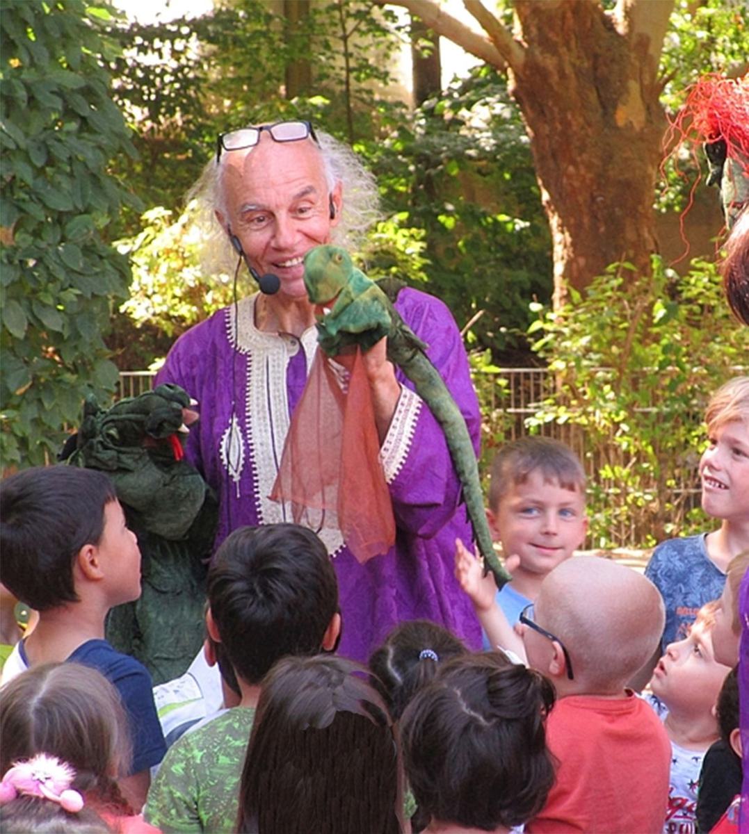 Micha im lila Gewand mit Drachenpuppe, lachend zwischen Kindern