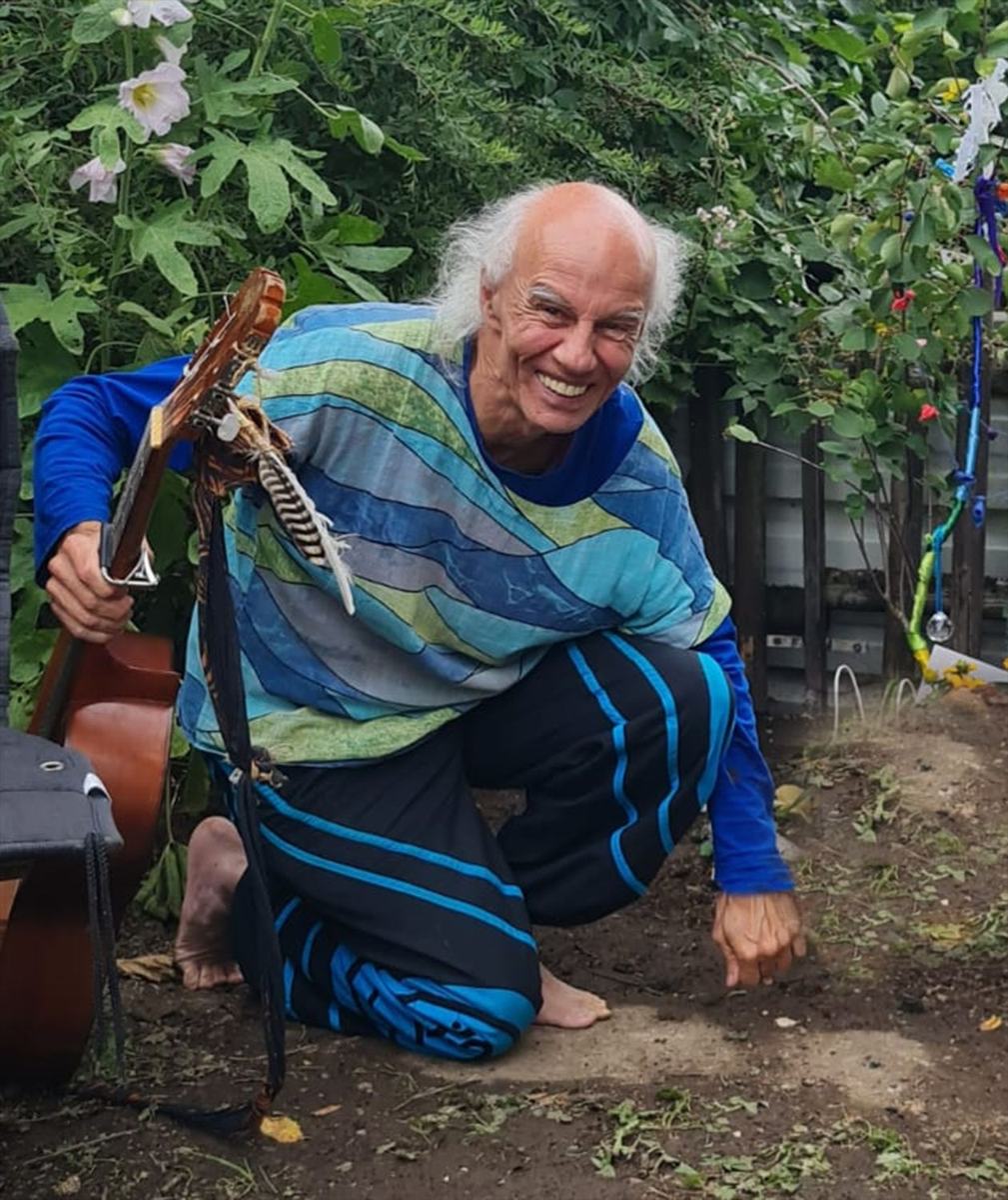 Micha kniet lachend im Garten, die Gitarre in der Hand, und schaut dich an