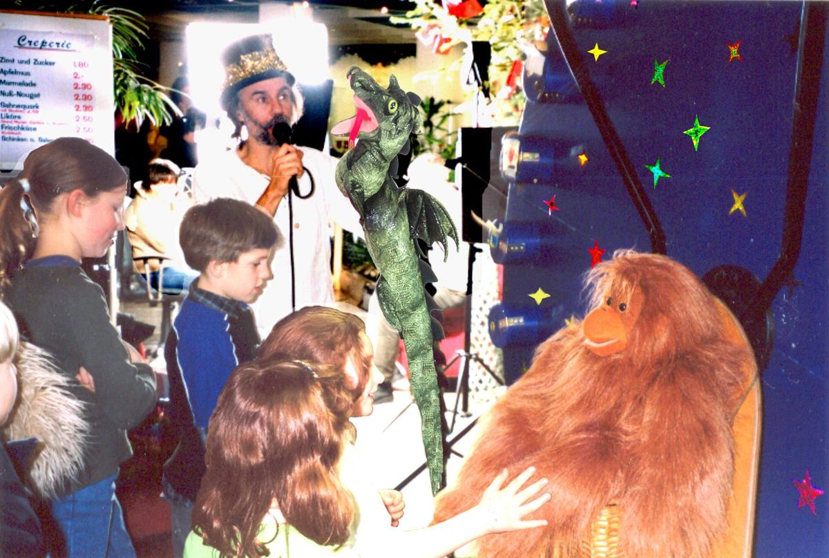 Micha mit Zylinder und Mikrofon, daneben ein Drache und ein Orang-Utan als Puppen, Kinder schauen zu